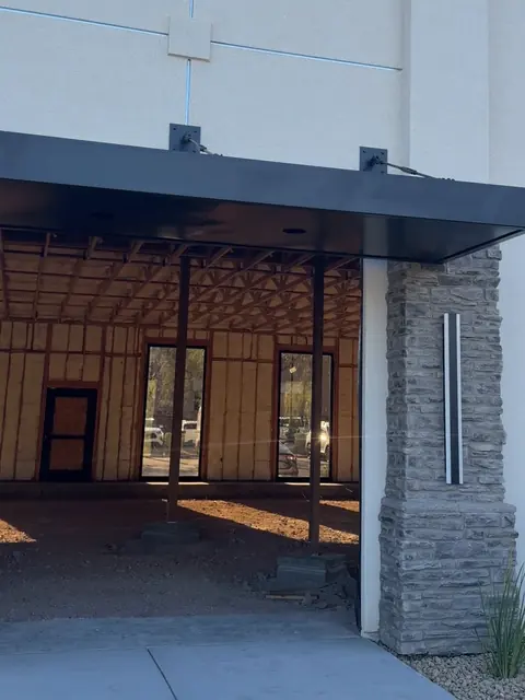 Finished stucco exterior of The Industry Studios with black entry awning and stone column, Henderson NV, May 2026
